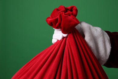 Photo of Santa Claus with red bag of Christmas gifts on green background, closeup