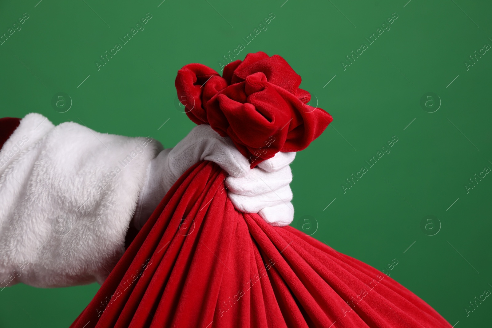 Photo of Santa Claus with red bag of Christmas gifts on green background, closeup