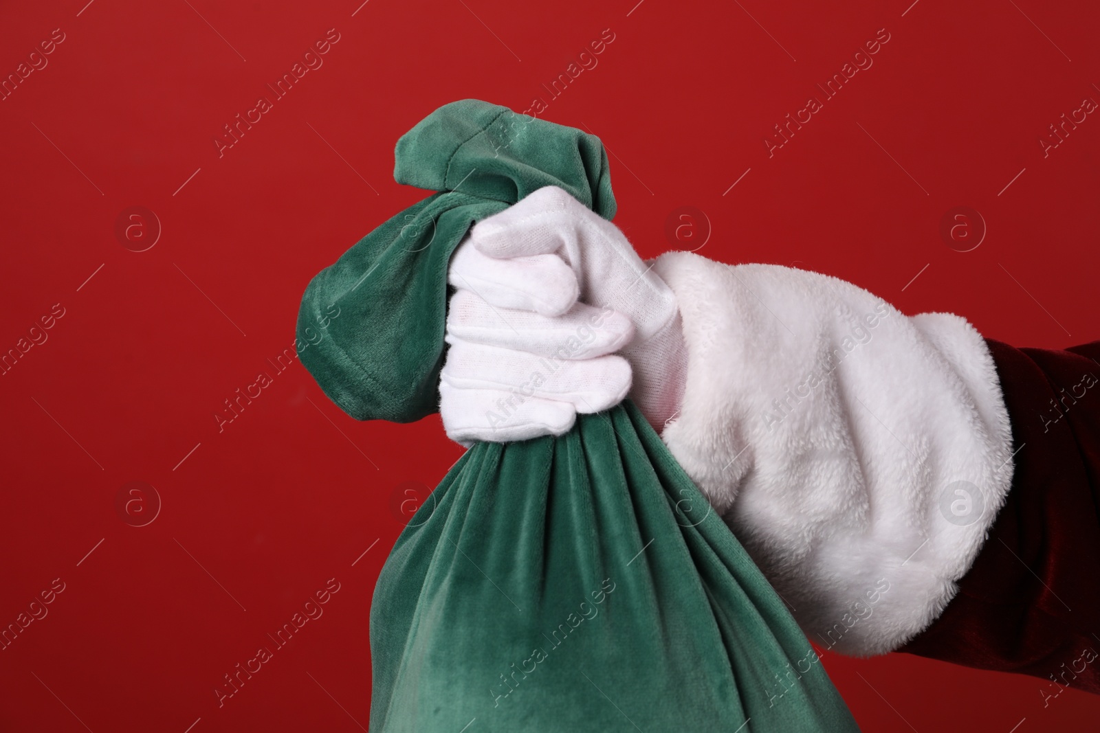 Photo of Santa Claus with green bag of Christmas gifts on red background, closeup