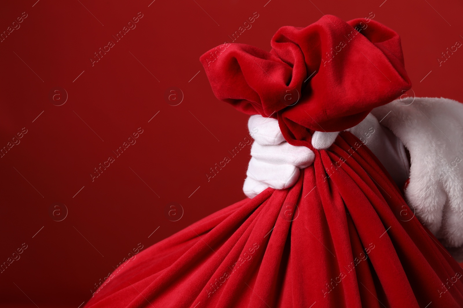 Photo of Santa Claus with bag of Christmas gifts on red background, closeup