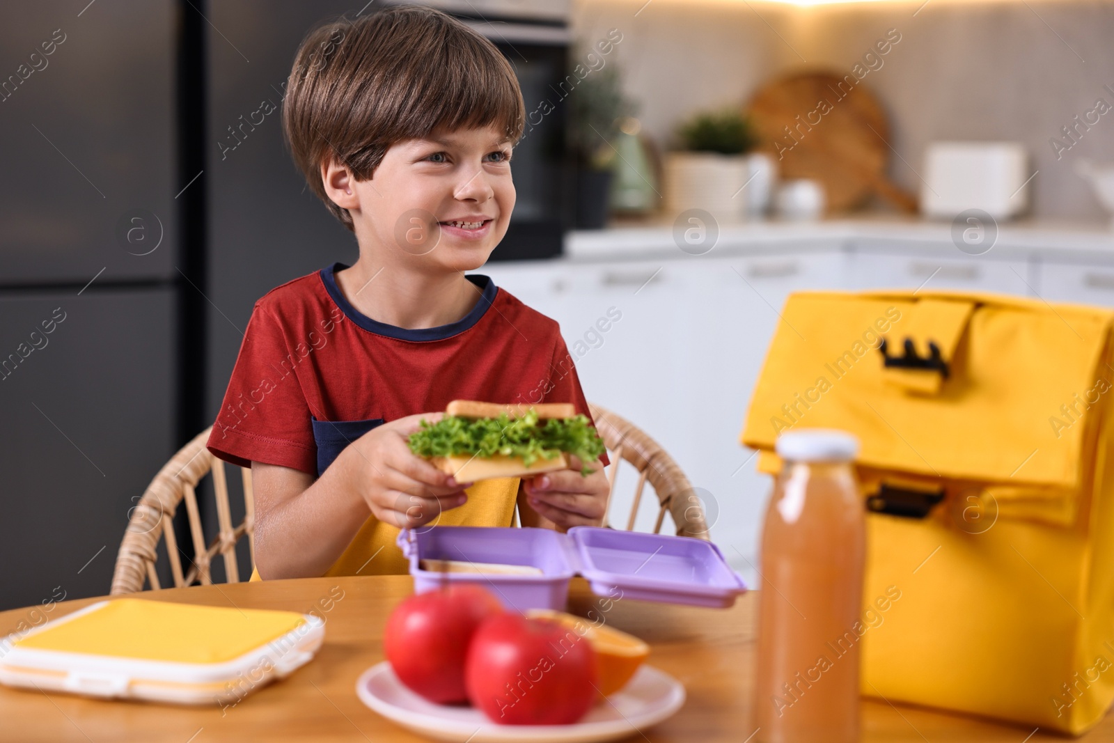 Photo of Cute boy with lunch box, healthy products and bag at wooden table in kitchen