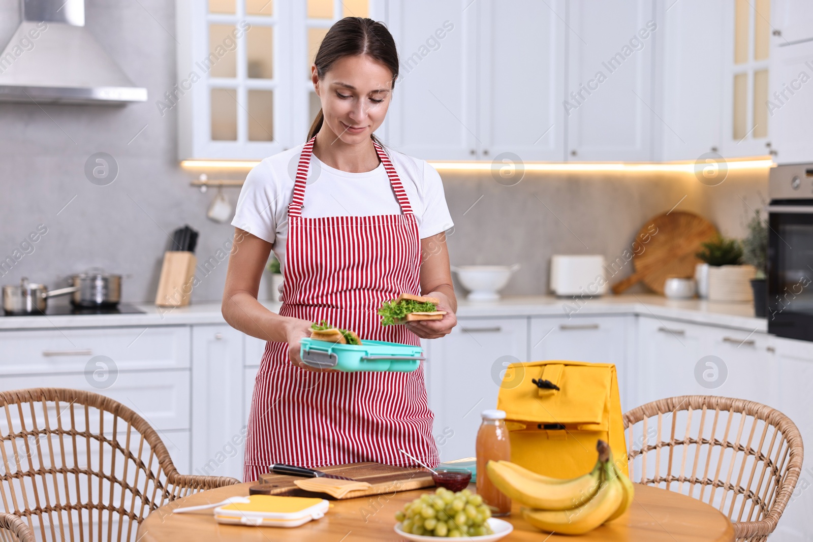 Photo of Woman packing school lunch box with healthy snacks at wooden table in kitchen