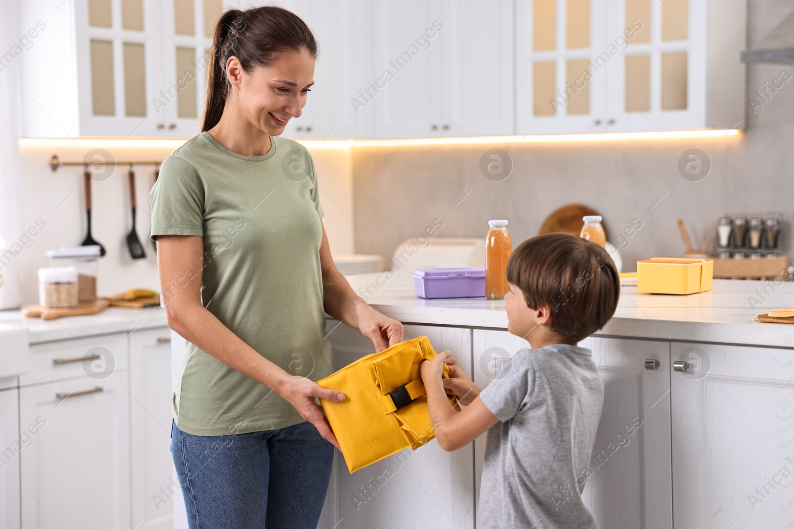 Photo of Smiling mother giving lunch bag to her son in kitchen