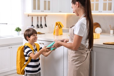 Mother giving lunch box to her son in kitchen. Preparing for school