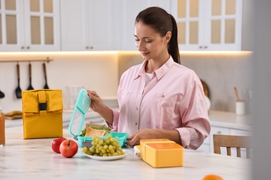 Photo of Woman packing school lunch box with healthy food at white marble table in kitchen