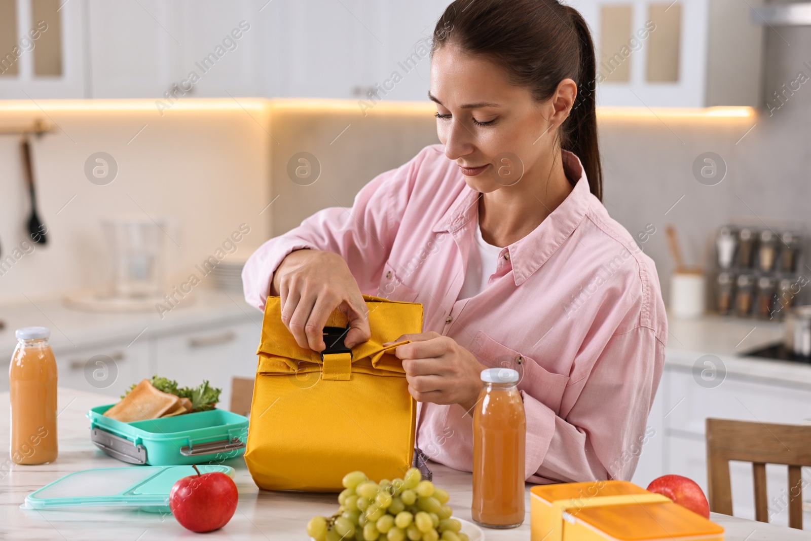 Photo of Woman with bag packing school lunch box and healthy food at white marble table in kitchen