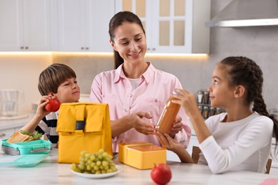 Photo of Mother and her children preparing school lunch boxes with healthy food at table in kitchen