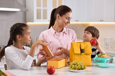 Photo of Mother and her children preparing school lunch boxes with healthy food at table in kitchen