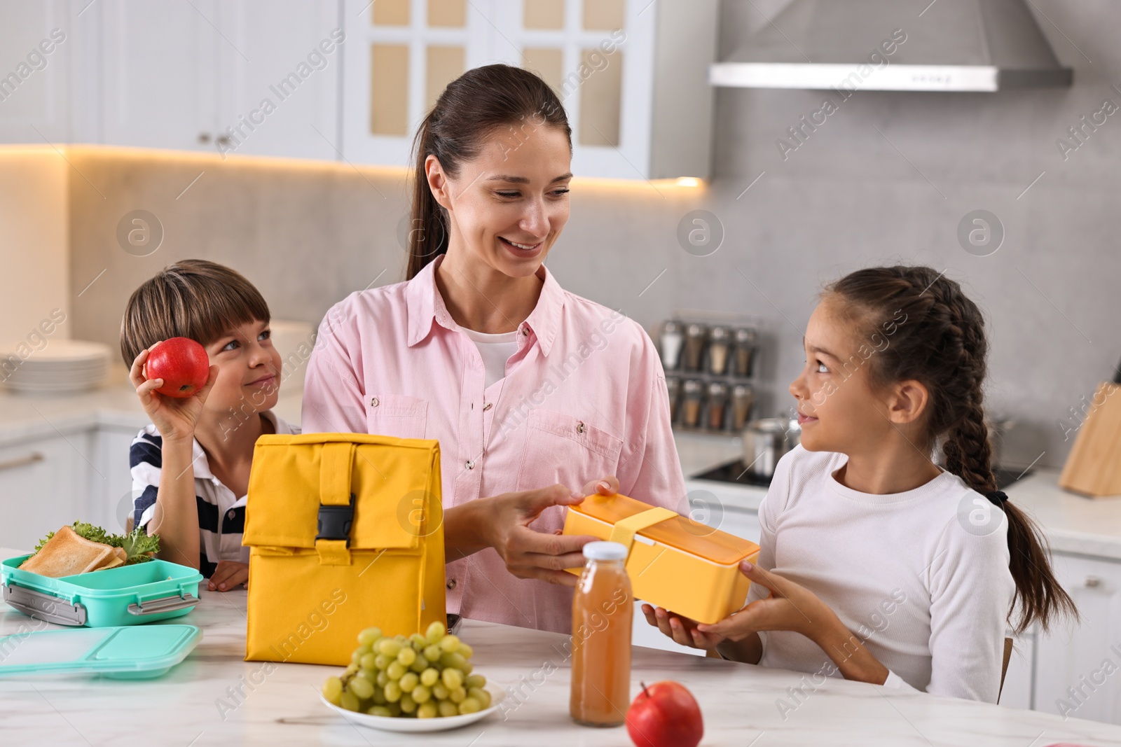 Photo of Mother and her children preparing school lunch boxes with healthy food at table in kitchen