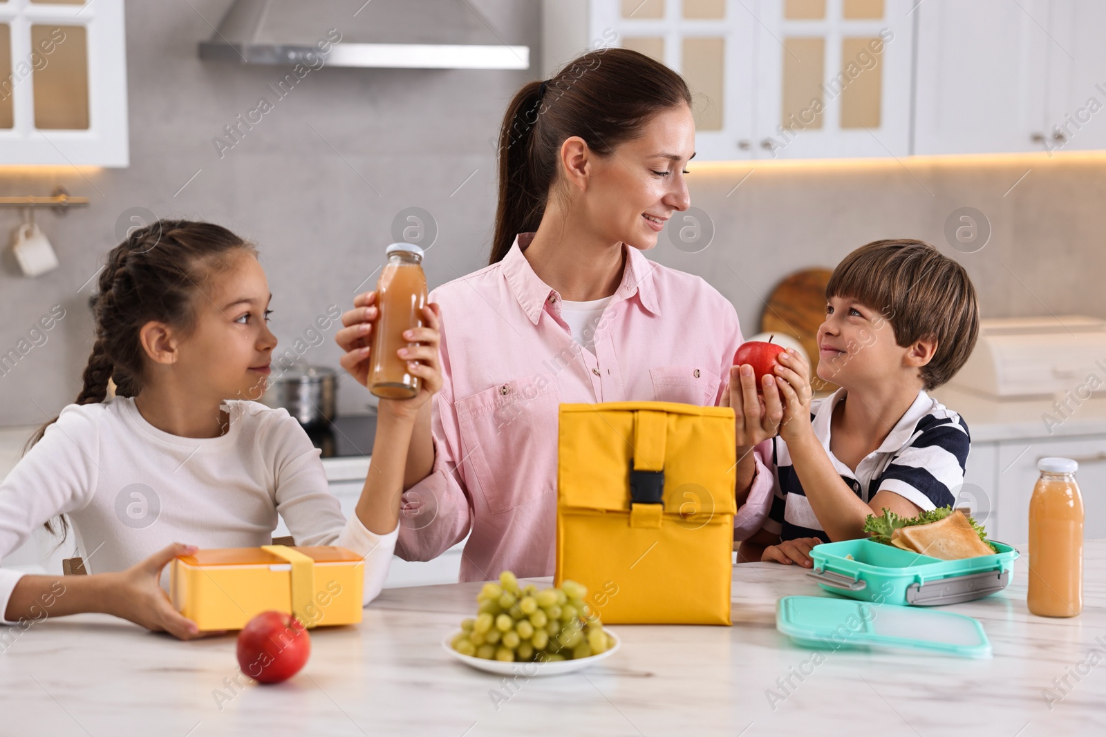 Photo of Mother and her children preparing school lunch boxes with healthy food at table in kitchen