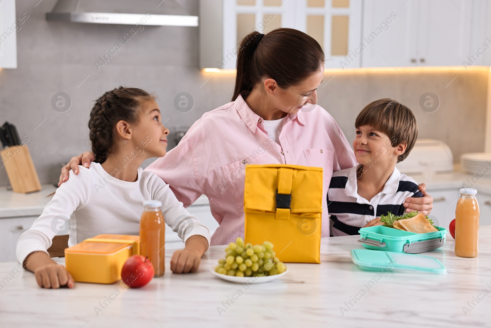 Photo of Mother and her children preparing school lunch boxes with healthy food at table in kitchen