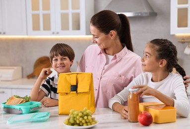 Mother and her children preparing school lunch boxes with healthy food at table in kitchen