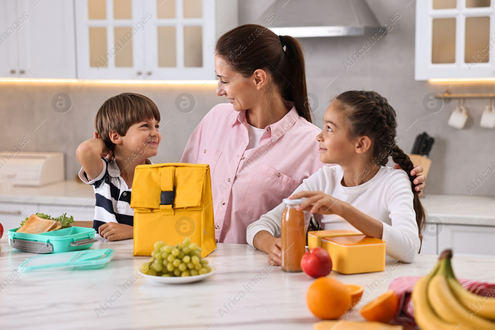 Photo of Mother and her children preparing school lunch boxes with healthy food at table in kitchen