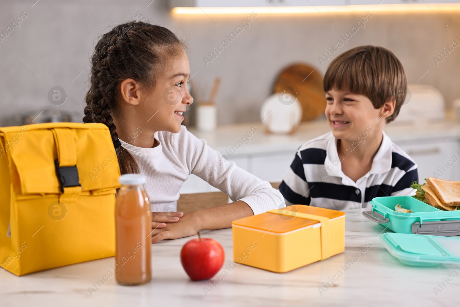 Photo of Cute children preparing school lunch boxes with healthy food at white marble table in kitchen