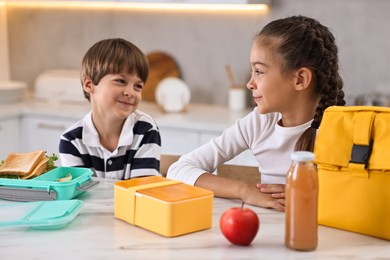 Photo of Cute children preparing school lunch boxes with healthy food at white marble table in kitchen