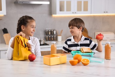 Cute children preparing school lunch boxes with healthy food at white marble table in kitchen