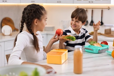 Photo of Cute children preparing school lunch boxes with healthy food at white marble table in kitchen