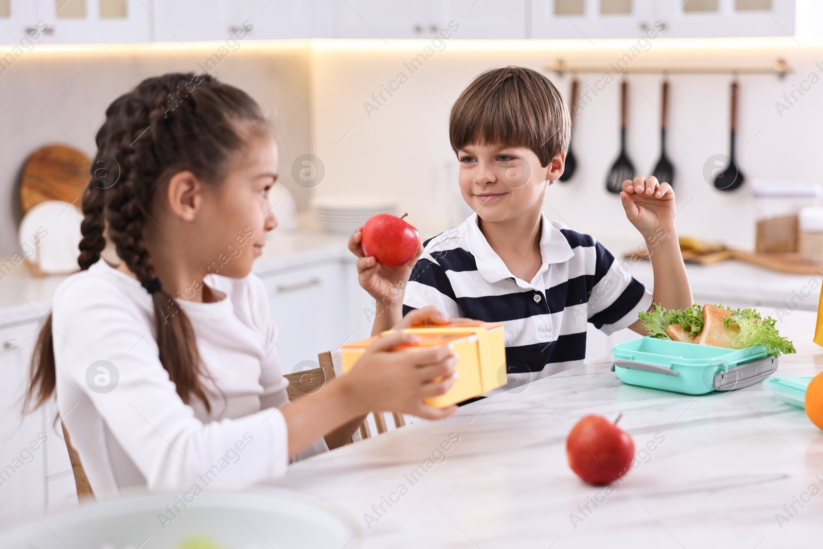 Photo of Cute children preparing school lunch boxes with healthy food at white marble table in kitchen