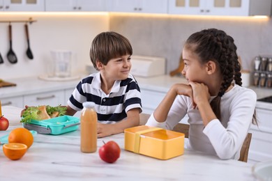 Photo of Cute children preparing school lunch boxes with healthy food at white marble table in kitchen