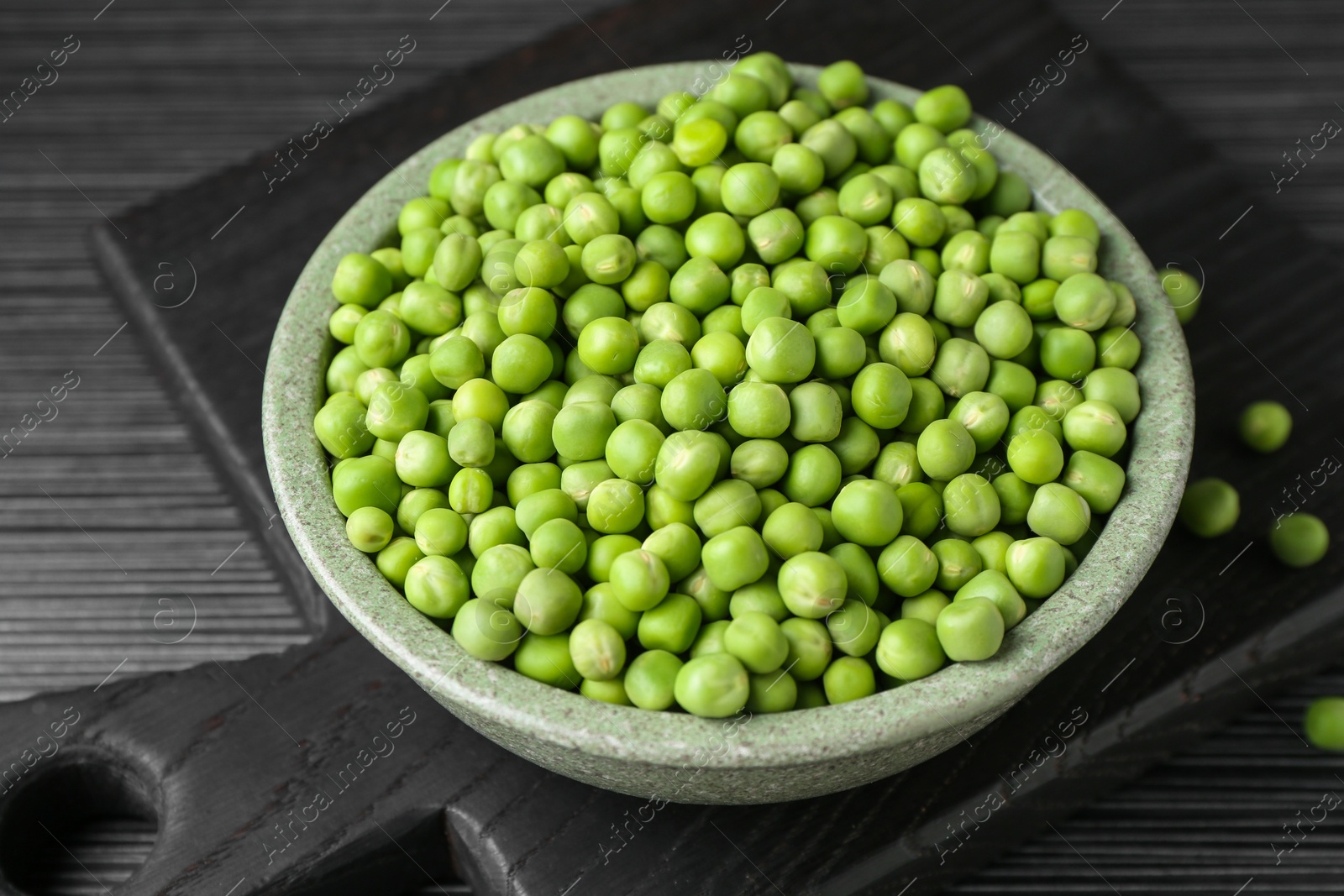 Photo of Fresh green peas in bowl on black wooden table, closeup