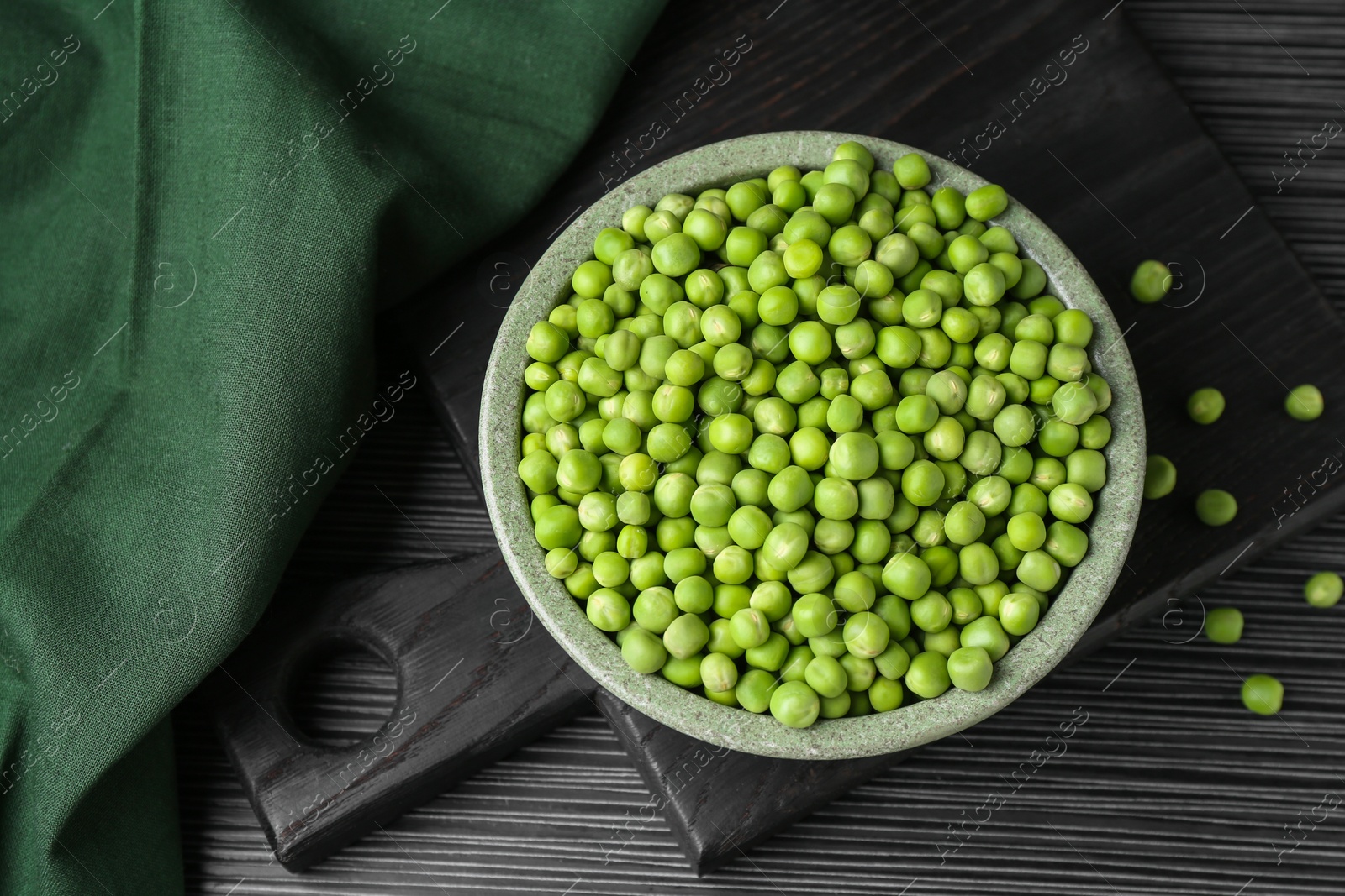 Photo of Fresh green peas in bowl on black wooden table, top view