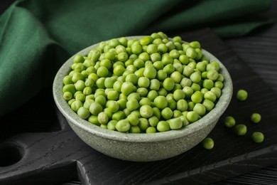 Photo of Fresh green peas in bowl on black wooden table, closeup