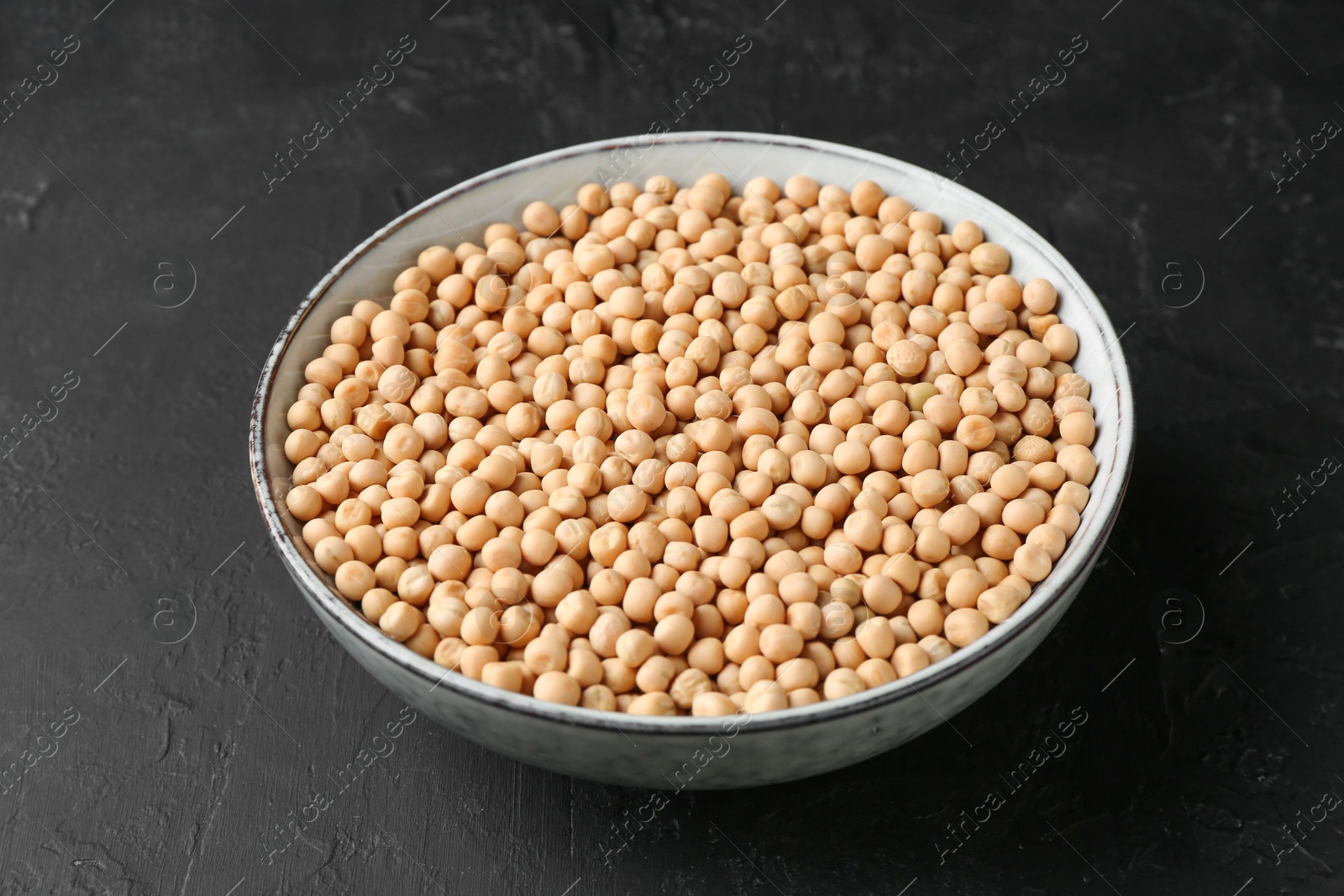 Photo of Dried peas in bowl on dark textured table, closeup