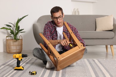 Photo of Man repairing wooden stool with screwdriver indoors