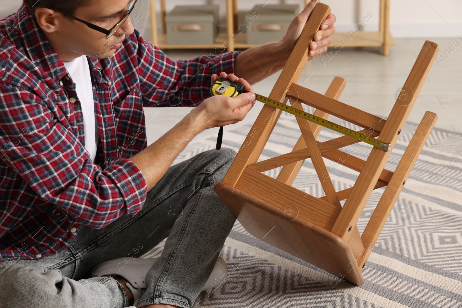 Photo of Man using tape measure while repairing wooden stool indoors