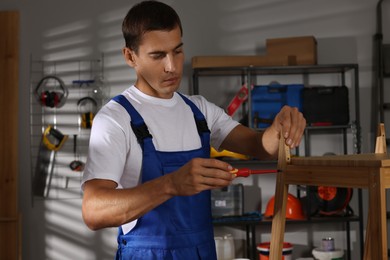 Photo of Man repairing wooden stool with screwdriver indoors