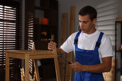 Man repairing wooden stool with hammer indoors