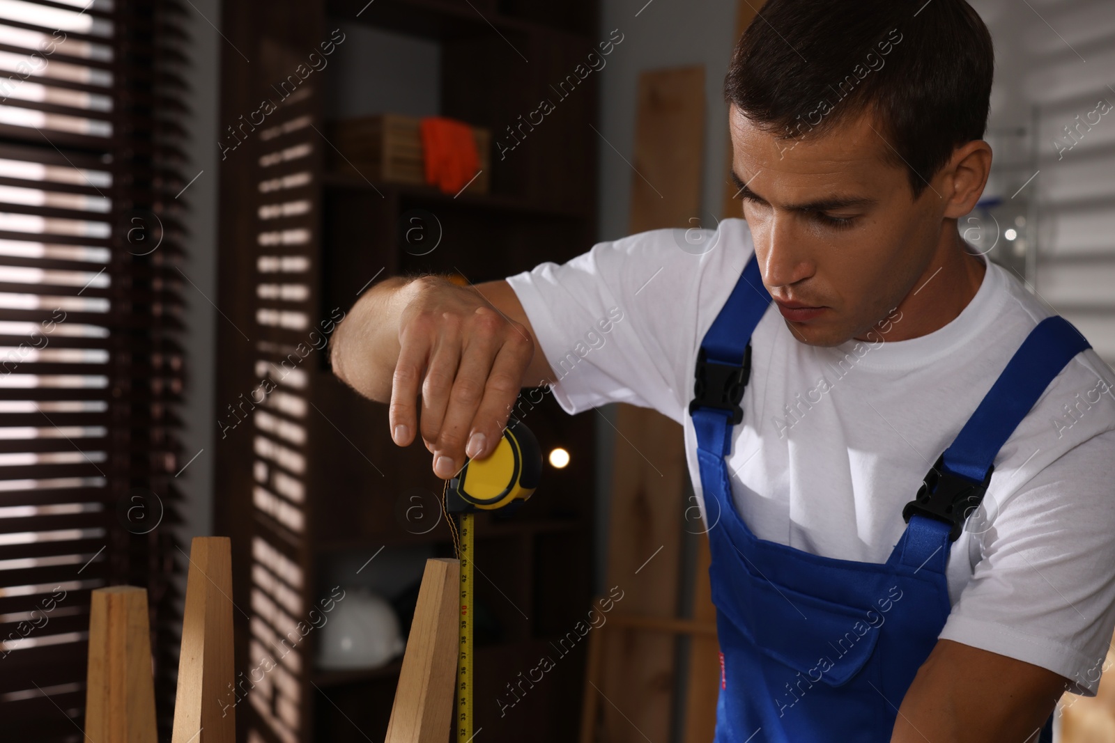 Photo of Man using tape measure while repairing wooden stool indoors