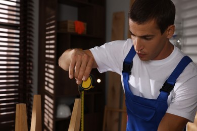 Man using tape measure while repairing wooden stool indoors