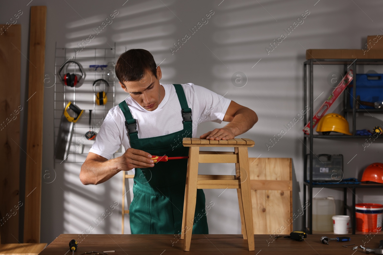 Photo of Man repairing wooden stool with screwdriver indoors