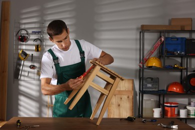 Photo of Man repairing wooden stool with screwdriver indoors