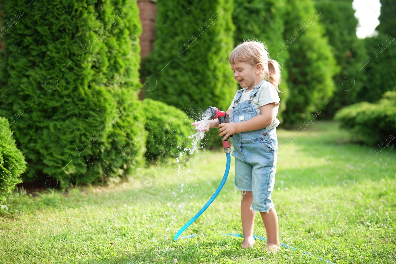 Photo of Little girl watering lawn with hose in backyard, space for text