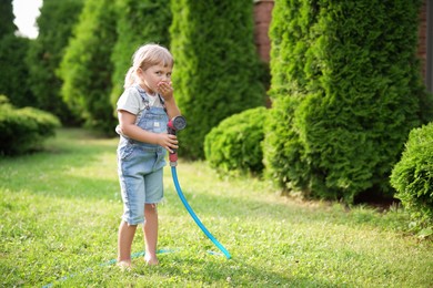 Little girl with hose in backyard, space for text