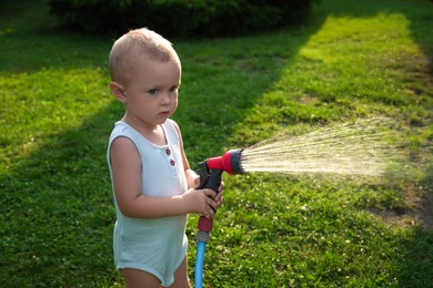 Photo of Little boy watering lawn with hose in backyard