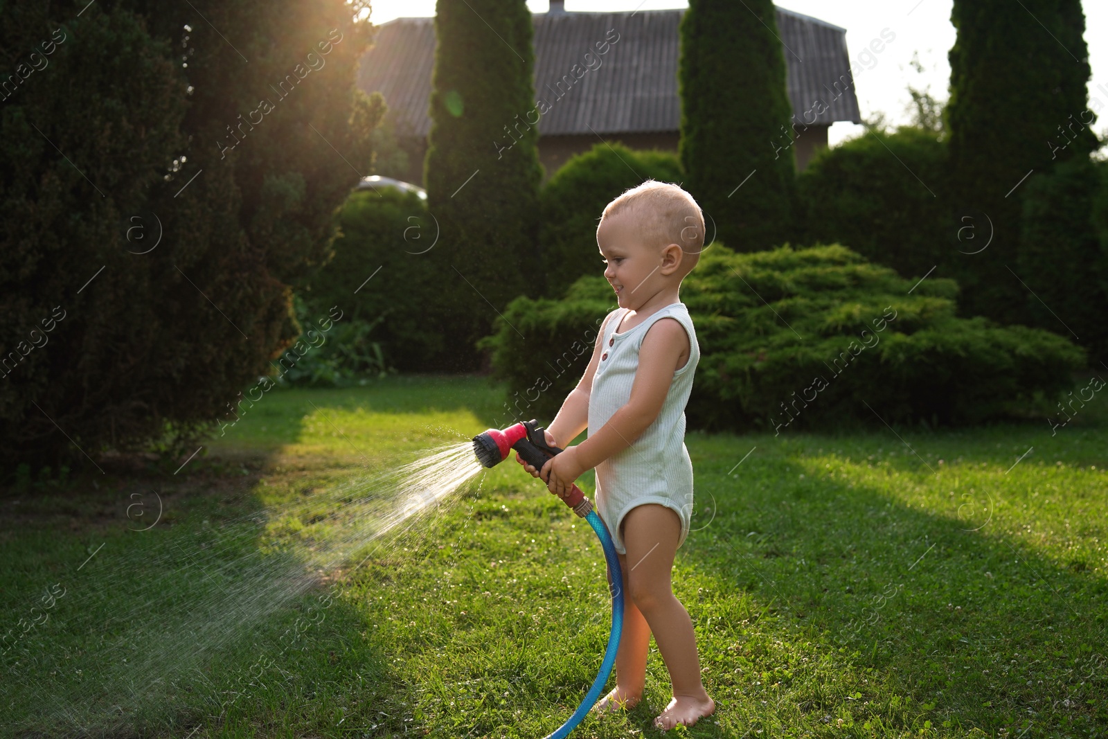 Photo of Little boy watering green grass on lawn in backyard