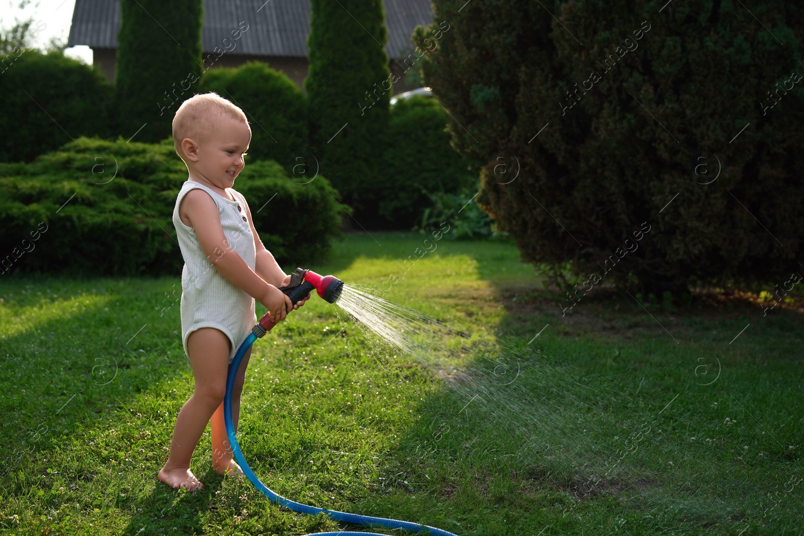 Photo of Little boy watering green grass on lawn in backyard