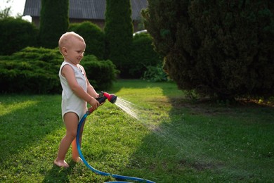 Little boy watering green grass on lawn in backyard