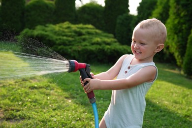 Photo of Little boy watering lawn with hose in backyard