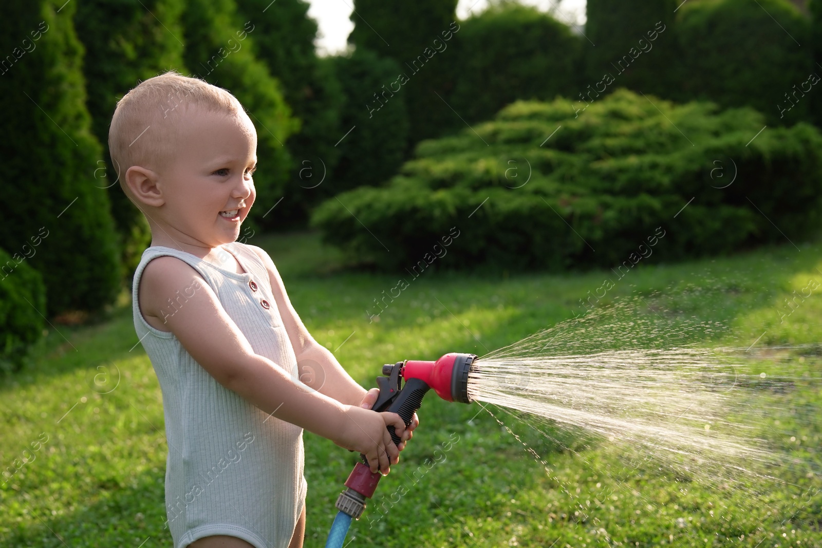 Photo of Little boy watering lawn with hose in backyard