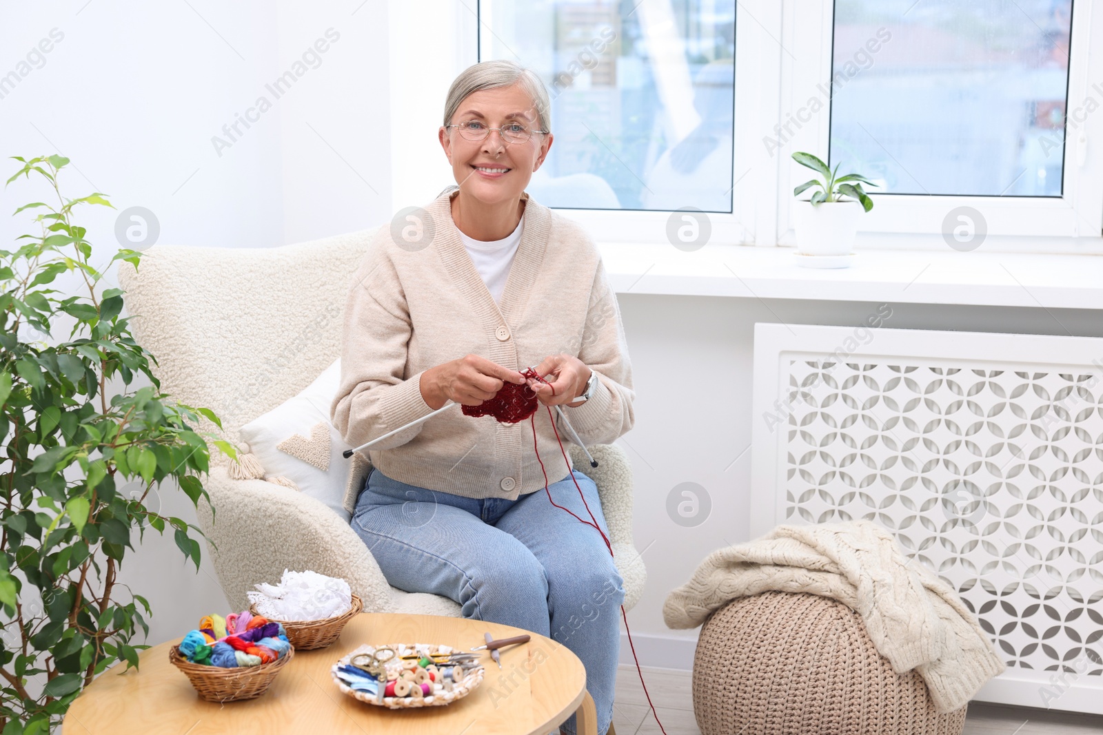 Photo of Smiling senior woman knitting on armchair at home