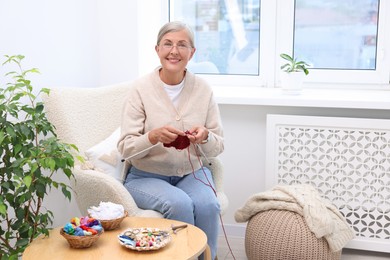 Smiling senior woman knitting on armchair at home