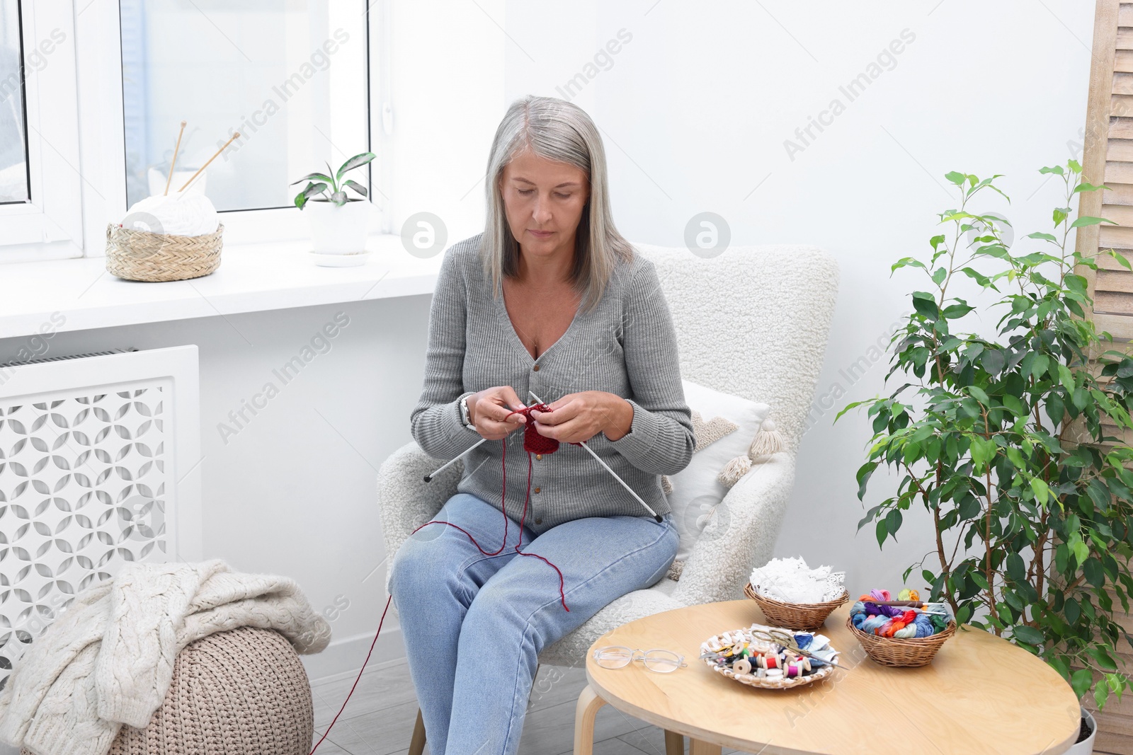 Photo of Beautiful senior woman knitting on armchair at home