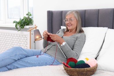 Smiling senior woman knitting on bed at home