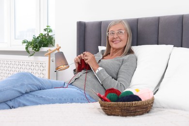 Smiling senior woman knitting on bed at home