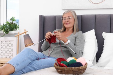 Beautiful senior woman knitting on bed at home