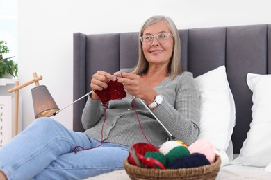 Smiling senior woman knitting on bed at home